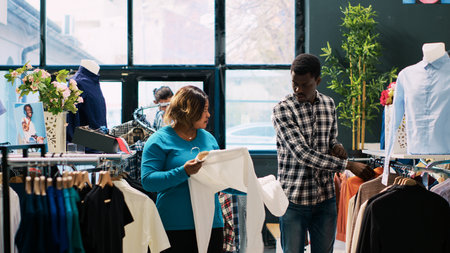 African american couple looking at fashionable clothes, checking items material in clothing store. Cheerful clients enjoying shopping session, buying stylish merchandise and accessories in modern boutiqueの写真素材