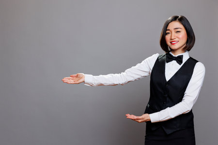 Catering service asian woman employee pointing with hands to right portrait. Smiling young attractive waitress extending arms to side, promoting product and looking at cameraの写真素材