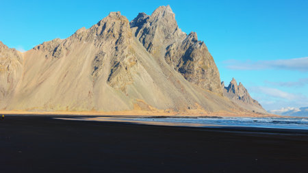 Vestrahorn mountains on arctic peninsula with natural black sand beach and beautiful skyline, sightseeing adventure. Ocean coastline shore and hills forming majestic landscape. Handheld shot.の写真素材