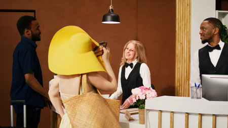Front desk team greeting travellers at hotel, welcoming guests at reception to review room reservation. Couple feeling excited about tropical summer vacation upon thier arrival. Handheld shot.の写真素材