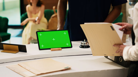 Guest asking about greenscreen info, pointing at tablet on reception counter in hotel lobby....