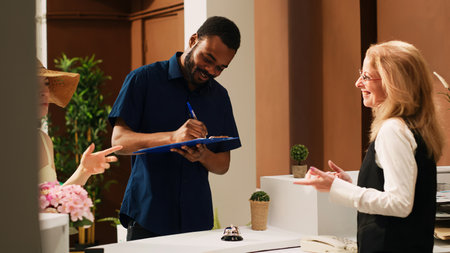 Happy couple checking in at hotel, signing registration papers before receiving access to room. People reading check in documents and confirming booking reservations. Handheld shot.の写真素材