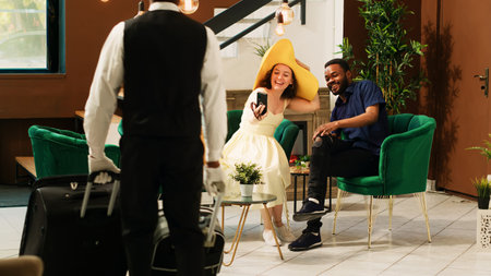 Guests using videocall meeting in hotel reception lobby, talking to someone on online videoconference in lounge area. Couple enjoying remote teleconference at tropical resort. Tripod shot.の写真素材