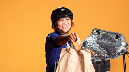 Close up shot of courier arriving to customer address, taking meal bag out of thermic backpack. Happy BIPOC bike rider delivering lunch to client, isolated over studio backgroundの写真素材