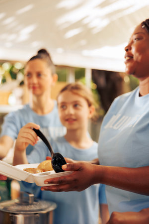 Close up view of women volunteering at food drive by serving hot meals with kindness to the homeless people. Detailed shot of female charity workers preparing food donations for the less fortunate.の写真素材