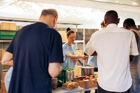 Image showcasing homeless people receiving warm meals and necessities from generous volunteers. Charity workers distributing free food to group of needy, less privileged, hungry individuals.の写真素材