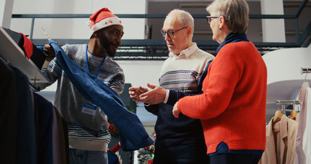 Elderly couple in festive shopping mall fashion boutique, being helped by friendly retail assistant...