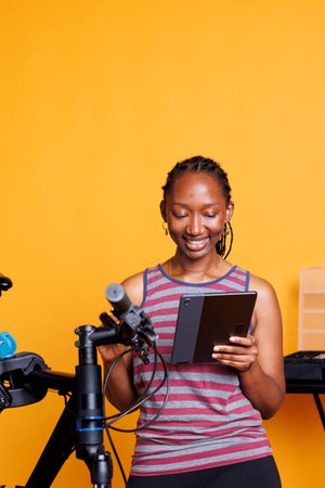 Youthful black woman examining broken bicycle and researching repair solutions on smart device. Image showing african american female holding a tablet and inspecting damaged bike components.の写真素材