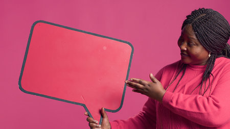 African American beauty holding a red speech bubble mockup for text messages and notes in her right hand. Black lady nodding in agreement with the content of the word-bubble copyspace template.の写真素材