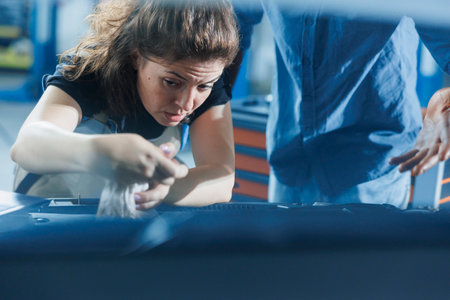 Hardworking repairman in garage finishing mending car, looking underneath vehicle hood to remove remaining oil leaks. Employee does annual engine cleaning on customer automobile in auto repair shopの写真素材