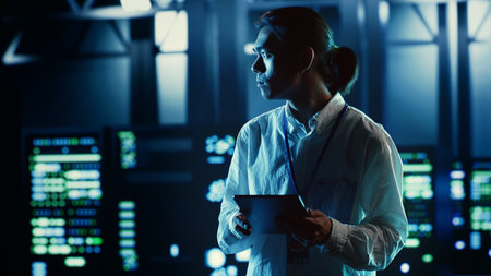 Asian employee walking through data center equipment clusters providing processing resources for...