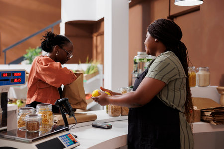 African American woman and female seller stand at local market surrounded by fresh produce and...