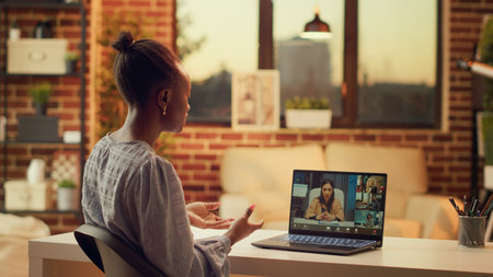 Worker chatting with clients on videocall, talking about price list and services to build online career in freelancing job. Woman using teleconference remote call at home, sunset light.の写真素材