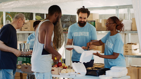 Multicultural volunteers distribute free food and essentials to the underprivileged. Voluntary people provide the less fortunate with humanitarian aid and hunger assistance in homeless shelters.の写真素材