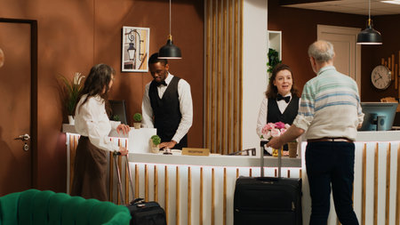 Retired couple arrive at hotel reception, talking to front desk staff before working on check in...