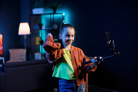 Popular kid uses cellphone on selfie stick to do viral dance for internet audience while listening to popular hit song. Young entertainer using mobile phone to film dancing video on viral musicの写真素材