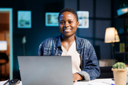 Black woman working at her laptop in a modern apartment, studying online and researching information...