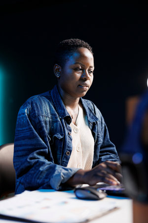 Focused African American woman at desk, using a laptop in her apartment. Busy browsing and typing, she works or studies online, dedicated and concentrated on her project or thesis.の写真素材