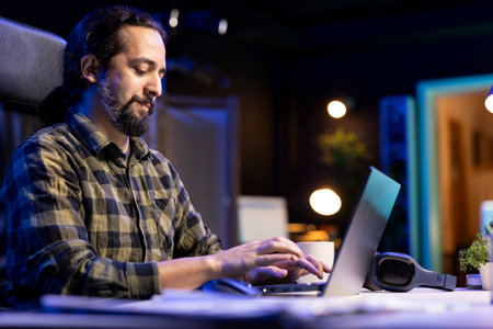 Man using a laptop to type and browse the internet at his living room desk. Young male adult is...