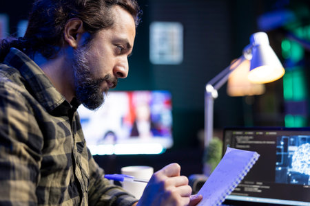 Closeup of man working on laptop, using AI to develop a futuristic software and taking down notes. Male individual writing new code in his notebook, showing his skill in programming and cyber securityの写真素材