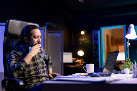 Male person looking at laptop screen displaying stock charts and statistics. Man covering mouth while analyzing financial information on his device, concentrated expression when checking market trendsの写真素材