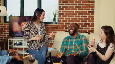 Hilarious asian woman telling jokes at apartment party, making friends laugh. Guest making happy BIPOC group of people chuckle in cozy house while drinking alcohol and eating appetizersの写真素材