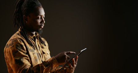 Model holding mobile tablet to check websites over black background, using device to browse through...