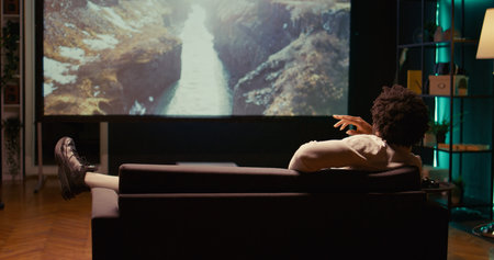 African american man watching nature documentary with beautiful cinematography on video projector....