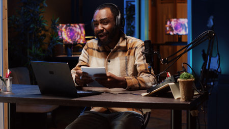 Influencer arriving in studio, reading outlined ideas from notebook to film vlog channel intro for online streaming platforms. Happy man starting vlogging session, following discourse script on paperの写真素材