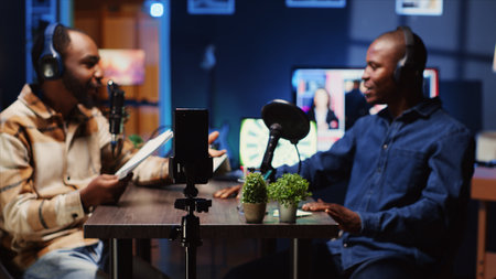 Man on podcast filming with smartphone on tripod while talking with guest during marathon stream for humanitarian cause. Host gathering donations from viewers during internet show, filming with phoneの写真素材