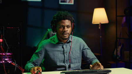 Sad gamer removing headphones in frustration, raging after game over screen while playing on computer desktop. African american man spamming keyboard buttons, struggling to win level on PC videogameの写真素材