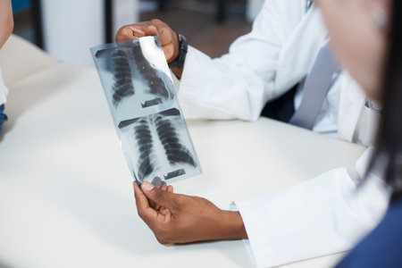 Close-up shot of doctor analyzing a radiography scan results with child and mother in medical cabinet. Specialist looks at x ray to give health care diagnosis to patients at consultation.の写真素材