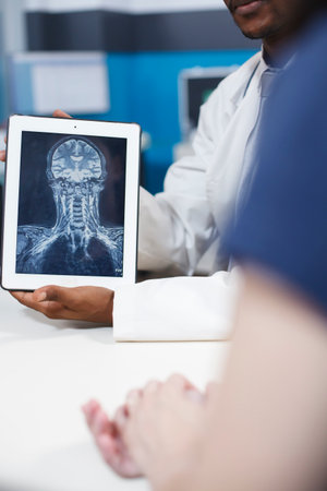 Close up of X ray result on digital tablet in healthcare office. Black doctor holding digital device with radiography of brain and bones indicating possible tumors or severe diseases and symptoms.の写真素材