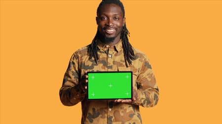 Male model holding laptop with greenscreen layout in studio, posing with isolated display copyspace on pc. Young adult presenting computer with blank mockup template on camera.の写真素材