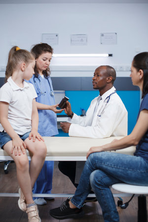 Doctor gives prescription pills bottle to assistance nurse in medical office. Caucasian mother with young girl at healthcare office receiving treatment from pediatrician, getting advice on medication.の写真素材