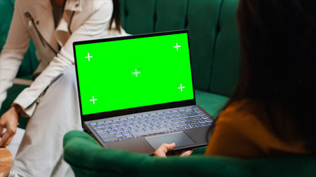 Hotel guest using laptop with greenscreen layout in lobby, looking at copyspace chromakey display in lounge area. Modern person holding pc showing isolated mockup template on screen.の写真素材