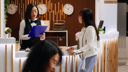 Hotel guest signing registration papers at front desk, confirming room reservation and enjoying five star resort facilities. Asian woman finishing with check in process, concierge services.の写真素材