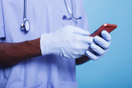 African American physician with selective focus, holding smartphone in blue scrubs, specializing in...