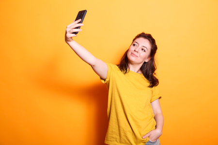Beautiful caucasian lady taking a selfie with her cellphone in a studio. Youthful woman capturing...