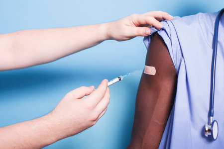 Close-up of medical nurse being vaccinated in studio by doctor. Medic uses syringe with needle to...