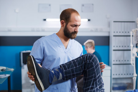 Close-up of orthopedic nurse assisting patient with knee injury at physical therapy. Male medical specialist providing osteopathy care to a man suffering from leg muscular discomfort.の写真素材