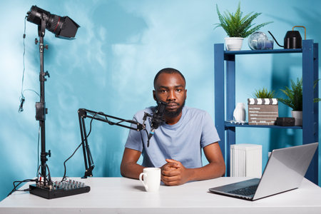 African american blogger recording vlog video and speaking in microphone portrait. Man streaming live on channel while creating digital content and looking at camera in home studioの写真素材