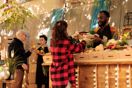 Farmers market vendor giving fresh organic produce box to customer, natural bio products. Woman...