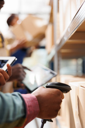 African american distribution warehouse worker arm scanning cardboard box code. Logistics manager cheking goods in stock using barcode scanner on freight parcels in storehouseの写真素材