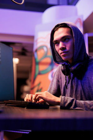 Asian hacker with smirk engaging in internet criminal activity while hacking server to steal...