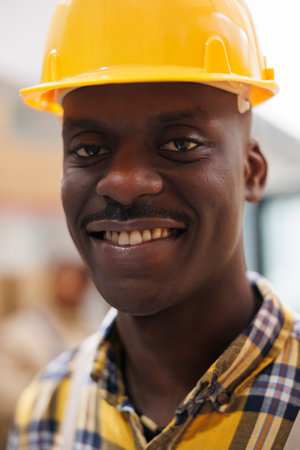Freight distribution african american smiling worker smiling face portrait. Young man wearing yellow safety industrial helmet looking at camera with optimistic facial expression in warehouseの写真素材