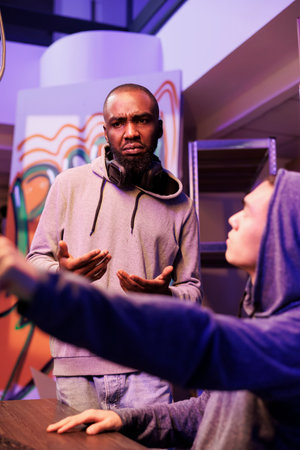 Hacker in hood pointing at illegal spyware code and asking developer for advice. Criminal showing crime partner malicious software on computer screen while cracking server passwordの写真素材