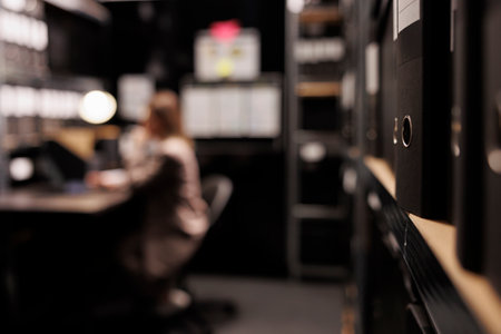 Selectiv focus of metallic storage full with investigation files, in background police officer analyzing crime scene evidence. Private detective working overtime at criminal case in arhive roomの写真素材