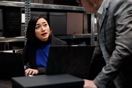 Professional administration employees imputing bookkeeping administrative data paperwork on laptop. Accountancy archival cabinet room filled with folders and diagram chartsの写真素材