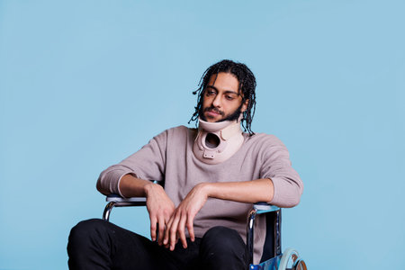 Exhausted arab man with neck brace sitting in wheelchair, healing from accident. Tired young patient wearing cervical collar protector for spinal injury recovering from traumaの写真素材